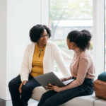 An educational counselor and a female student smiling while looking at a laptop together, illustrating the process of UCAS application support for international students.