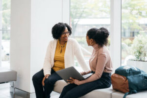 An educational counselor and a female student smiling while looking at a laptop together, illustrating the process of UCAS application support for international students.
