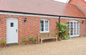 A side-view of a newly completed red-brick single-storey house addition with white timber doors and windows, representing a project used to estimate price in a home extension cost calculator UK.
