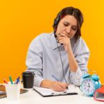 concentrated-young-call-center-girl-wearing-headset-sitting-desk-putting-hand-mouth-writing-isolated-orange (1) (2) (1)