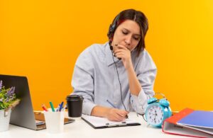 concentrated-young-call-center-girl-wearing-headset-sitting-desk-putting-hand-mouth-writing-isolated-orange (1) (2) (1)