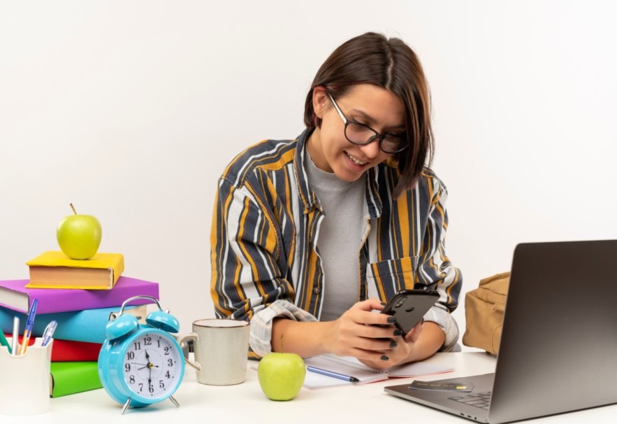 smiling-young-student-girl-wearing-glasses-sitting-desk-with-university-tools-using-mobile-phone-isolated-white-wall (1) (1) (1) (1) (1) (1)