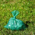A close up image of a full green plastic dog poop bag on a lush green lawn.