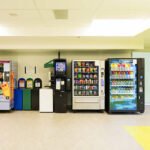 Various vending machines and trash cans lined up against a wall.
