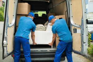 Two Male Workers In Blue Uniform Adjusting Sofa In Truck